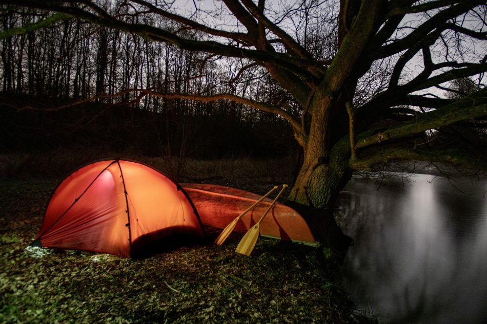 Ein von innen beleuchtetes Zelt am Fluss unter einer alten Eiche.